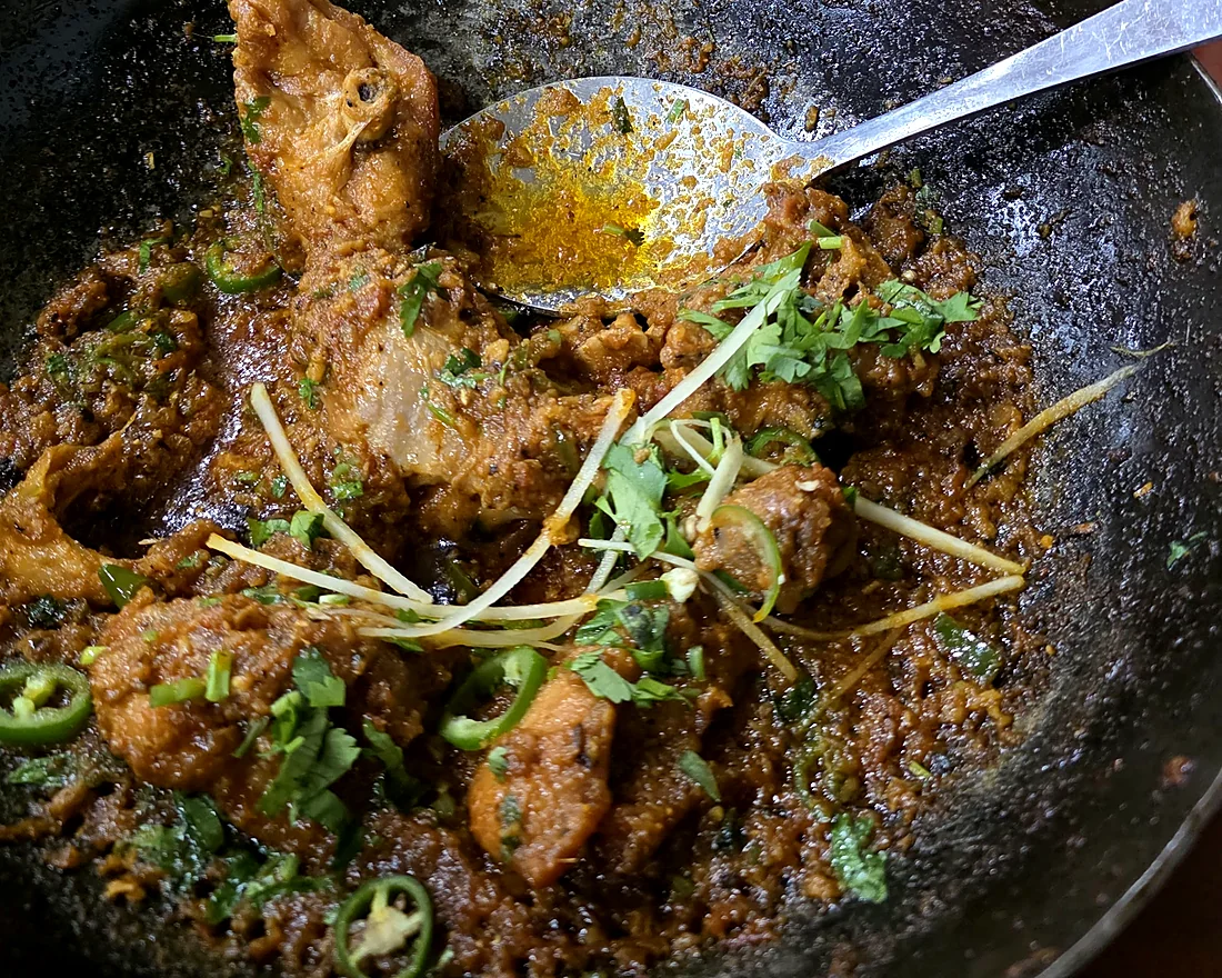Bone-in karahi in a black iron wok, garnished with ginger strips, green chilies and coriander