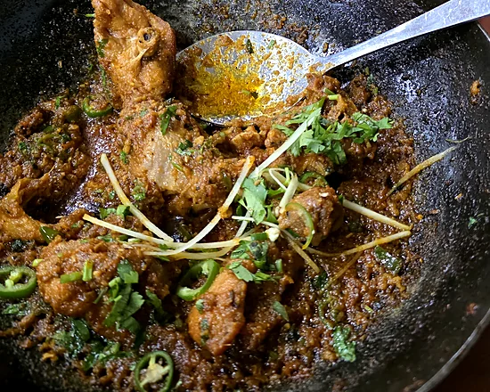 Bone-in karahi in a black iron wok, garnished with ginger strips, green chilies and coriander
