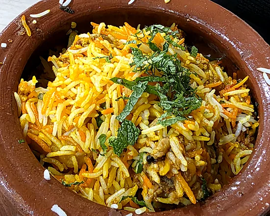 Biryani in a clay matka pot on a woven mat, saffron and white basmati rice topped with fresh mint