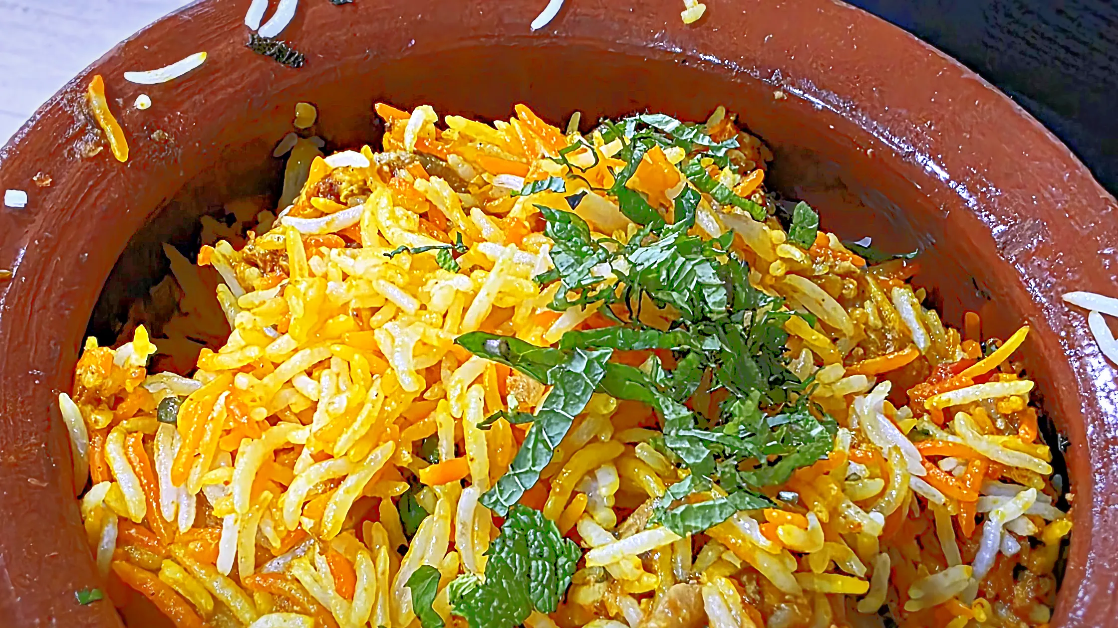 Close-up of biryani in a clay matka pot, saffron and white basmati rice topped with fresh mint
