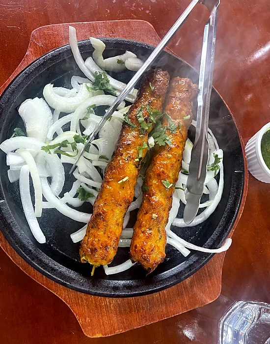 Chicken seekh kababs on a sizzling iron plate with onions
